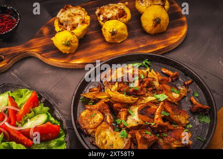 Pfifferlingen, gebraten mit Kartoffeln in einer gusseisernen Pfanne und gefüllte Kürbisse auf einem Holzbrett, Gemüse und eine burgunderrote Serviette auf einer grauen Stockfoto