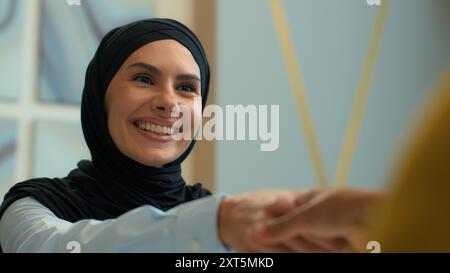 Glückliche lächelnde muslimische islamische Frau im Hijab Geschäftsfrau rekrutiert Kunden Handshake Arme weibliche Geschäftspartner Kollegen schütteln Hände Deal Stockfoto