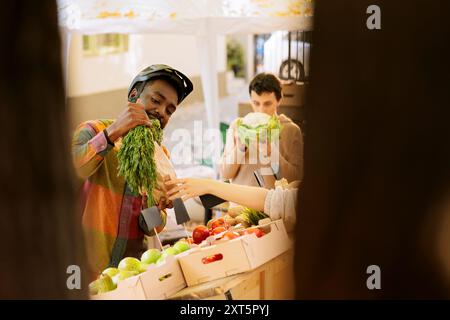 Selektiver Fokus auf schwarzen Lieferanten, der ein Paket mit frisch geernteten Produkten von lokalen Anbietern hält. Junger afroamerikanischer Kurier mit brauner Tasche mit saisonalem Bio-Gemüse. Stockfoto