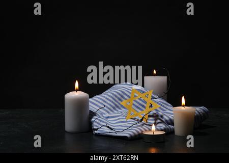 Gefangenenuniform, brennende Kerzen und David-Stern auf dunklem Hintergrund. Holocaust-Gedenktag Stockfoto