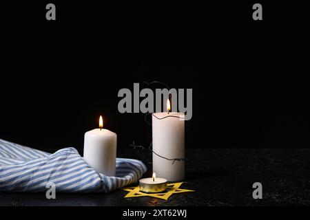 Gefangenenuniform, brennende Kerzen und David-Stern auf dunklem Hintergrund. Holocaust-Gedenktag Stockfoto