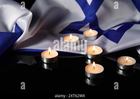 Brennende Kerzen und große Flagge Israels auf dunklem Hintergrund. Holocaust-Gedenktag Stockfoto