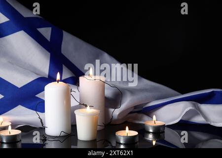 Brennende Kerzen mit Stacheldraht und großer Flagge Israels auf dunklem Hintergrund. Holocaust-Gedenktag Stockfoto
