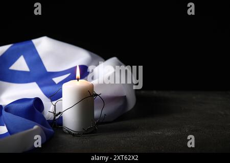 Brennende Kerze mit Stacheldraht und großer Flagge Israels auf dunklem Hintergrund. Holocaust-Gedenktag Stockfoto