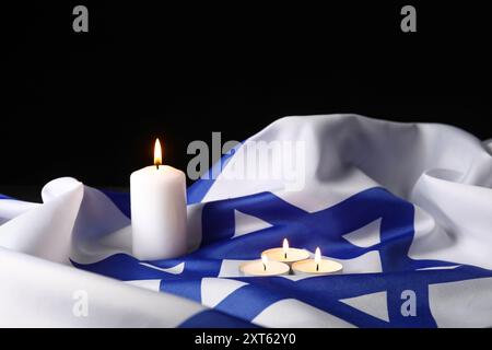 Brennende Kerzen und große Flagge Israels auf dunklem Hintergrund. Holocaust-Gedenktag Stockfoto
