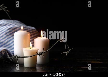 Gefangenenuniform, brennende Kerzen und Stacheldraht auf dunklem Hintergrund. Holocaust-Gedenktag Stockfoto