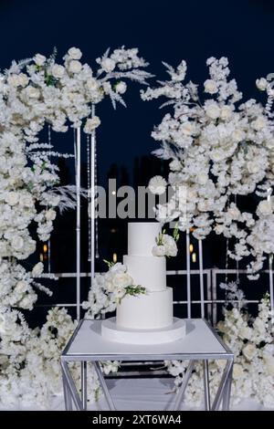 Hochzeitseinrichtung mit dreistufigem weißem Kuchen mit Blumenakzenten. Hochzeitsinspiriert, luxuriöse Veranstaltungen Stockfoto