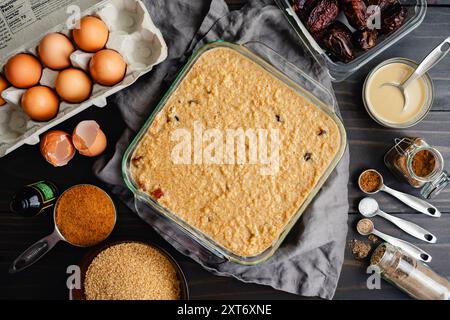 Ungekochtes Frühstück im Nahen Osten: Frühstücksauflauf mit Bulgur, Datteln, Eiern, Milch und Gewürzen in einer Glasbackform auf Holztisch Stockfoto