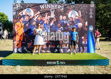 Atalanta-Fans posieren für ein Foto vor dem Siegerteam des UEFA-Cups 2024. Die Fans der spanischen Champions-League-Gewinner Real Madrid und der italienischen UEFA-Cup-Gewinner Atalanta trafen sich auf dem Kahla-Platz in Warschau neben der Weichsel zum UEFA-Super-Cup-Fanfestival. Im Vorgriff auf das Spiel am folgenden Tag stehen die Besucher an, um Fotos mit der Trophäe zu machen und an einer Reihe von Fußballspielen und -Aktivitäten teilzunehmen. Der UEFA-Supercup findet am 14. August 2024 im PGE Narodowy in Warschau statt und wird von den Gewinnern der Champions League und den Gewinnern des UEFA-Pokals bestritten. Stockfoto