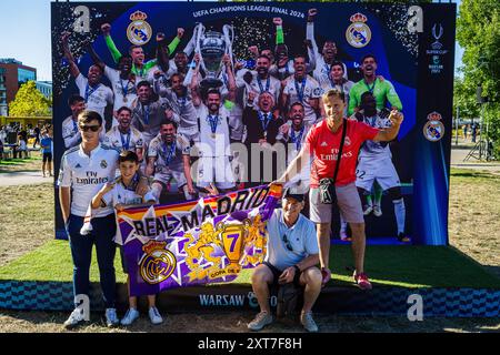 Die Fans von Real Madrid posieren für ein Foto vor dem Siegerteam der Champions League 2024. Die Fans der spanischen Champions-League-Gewinner Real Madrid und der italienischen UEFA-Cup-Gewinner Atalanta trafen sich auf dem Kahla-Platz in Warschau neben der Weichsel zum UEFA-Super-Cup-Fanfestival. Im Vorgriff auf das Spiel am folgenden Tag stehen die Besucher an, um Fotos mit der Trophäe zu machen und an einer Reihe von Fußballspielen und -Aktivitäten teilzunehmen. Der UEFA-Supercup findet am 14. August 2024 im PGE Narodowy in Warschau statt und wird von den Gewinnern der Champions League und des UEFA Cup wi bestritten Stockfoto