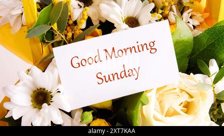 GUTEN MORGEN WELT auf einer weißen Karte in einem Korb voller Blumen Stockfoto