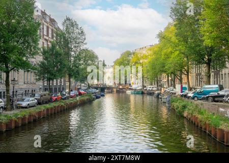 Niederlande. Ein Sommertag auf einem Kanal im Zentrum von Amsterdam. Viele Autos stehen auf den Böschungen. Mehrere Boote liegen auf dem Wasser Stockfoto