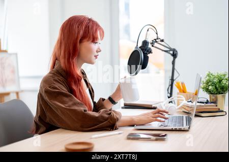 Eine selbstbewusste und schöne asiatische Podcasterin arbeitet in ihrem Heimstudio und genießt einen Kaffee, während sie eine neue Episode ihres Podcasts aufnimmt. Stockfoto