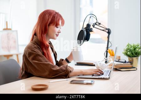 Eine selbstbewusste und schöne asiatische Podcasterin arbeitet in ihrem Heimstudio und genießt einen Kaffee, während sie eine neue Episode ihres Podcasts aufnimmt. Stockfoto