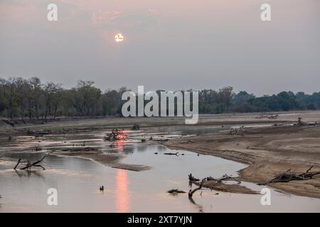 Die Morgensonne blickt durch die Wolken auf einer Kurve des Luangwa River mit Überresten von Bäumen von Überschwemmungen im North Luangwa National Park, Sambia Stockfoto