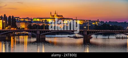 Die Jirasek-Brücke überquert die Moldau in Prag, auf der gegenüberliegenden Uferseite die Prager Burg beleuchtet. Die untergehende Sonne wirft ein warmes Licht auf die Stadtlandschaft und schafft eine ruhige und malerische Szene. Stockfoto