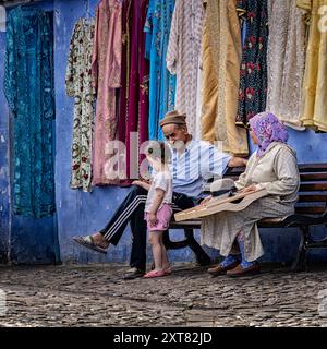 Chefchaouen, Marokko: Großvater und Großmutter mit Enkelin. Marokkanische Familie sitzt auf einer Bank in der blauen Stadt Medina. Stockfoto