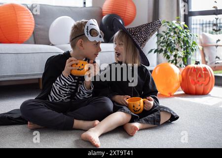 Mädchen und Junge Schulkinder sitzen auf dem Boden und halten Kürbisbecher Stockfoto