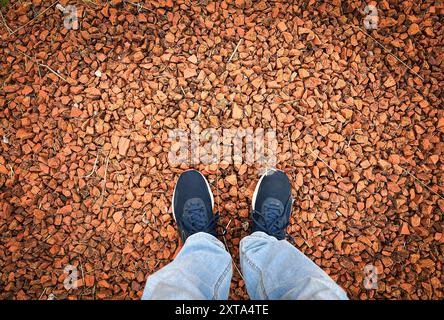 Bild von oben von zwei Füßen mit Turnschuhen auf einem Boden aus rötlichen Steinen. Selfie-Konzept. Stockfoto