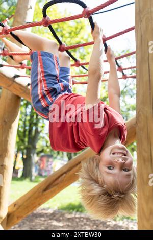 Lustiger Junge, 7 Jahre alt, hängt auf dem Spielplatz, auf den Kopf gestellt. Fröhliche Kindheit. Freude, Verwöhnung Stockfoto