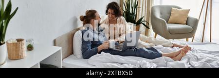 Ein Paar im Pyjama entspannt sich im Bett, genießt Kaffee und einen Laptop zusammen. Stockfoto