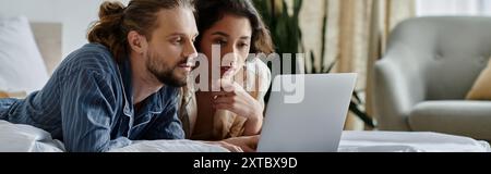 Ein liebevolles Paar kuschelt sich im Bett, während es einen Laptop ansieht. Stockfoto