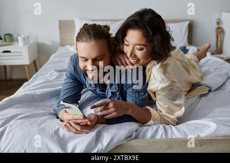 Ein Paar im Pyjama entspannt sich im Bett, lacht und schaut auf ein Telefon. Stockfoto