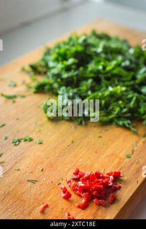 Haufen gehackter Petersilie und Chili-Pfeffer auf Holzbrett. Gehackte grüne Kräuter und rote Paprika auf Schneidebrett. Konzept für gesunde Ernährung. Stockfoto