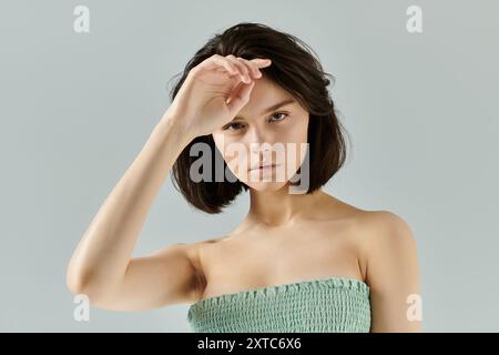 Eine Frau mit kurzen, dunklen Haaren posiert vor einem schlichten Hintergrund, ihre Hand schirmt ihre Augen ab. Stockfoto