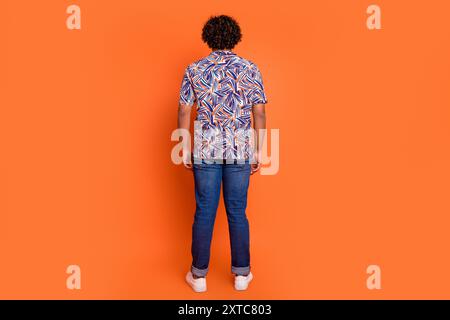 Foto in voller Länge von hübschem jungen Mann Rückansicht Shopping gekleidet stilvolle bunte Kleidung isoliert auf orangefarbenem Hintergrund Stockfoto