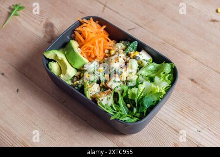 Eine Lunchbox aus Plastik mit Rosenkohl, gegrilltem Käse, Brokkoli-Stielen, Zuckermais, zerstoßenen Nüssen und Dressing. Zusammen mit Avocado, Karotten und gemischten Blättern. Stockfoto