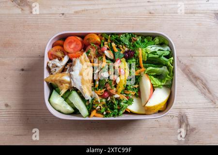 Eine Lunchbox aus Plastik mit hausgemachtem frischem Salat, Tomaten, geschnittenem Apfel und geräuchertem Makrelenfilet. Stockfoto