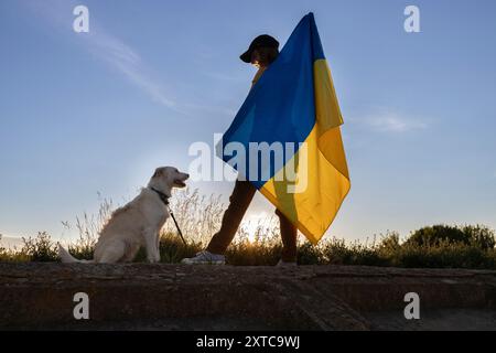 Silhouette eines weiblichen Hundes, der bei Sonnenuntergang die ukrainische Flagge am Himmel hält. Unabhängigkeitstag der Ukraine. Freiheit, Vertrauen, Stockfoto