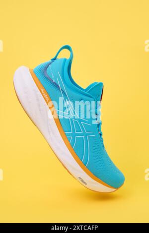 Einzelne blaue Asics Gel-Nimbus 25 Sportschuhe mit Schatten auf durchgehendem gelbem Hintergrund. Stylische Sneaker. Modisches minimalistisches Konzept, fliegender Schuh Stockfoto