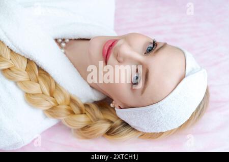 Eine Frau mit blondem Haar und blauen Augen liegt auf einem Bett mit einem weißen Gewand und einem weißen Haarband Stockfoto