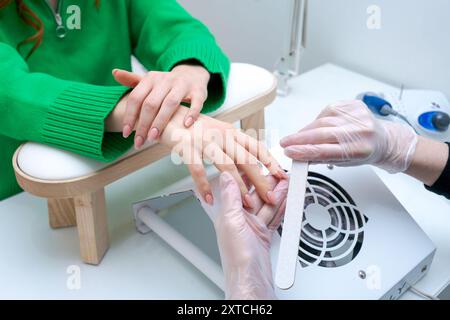 Eine Frau lässt ihre Nägel von einem Manikürer machen. Die Maniküre trägt Handschuhe und trocknet die Nägel der Frau mit einem Ventilator Stockfoto