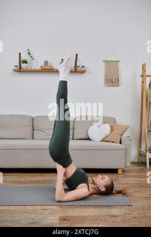 Eine junge Frau übt zu Hause Yoga und spielt eine Inversionspose auf einer Matte. Stockfoto