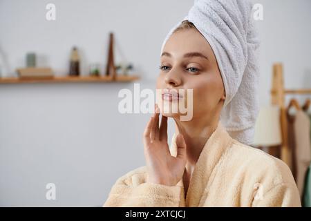 Frau im Bademantel mit handtuchumwickelten Haaren, wirkt zu Hause heiter. Stockfoto