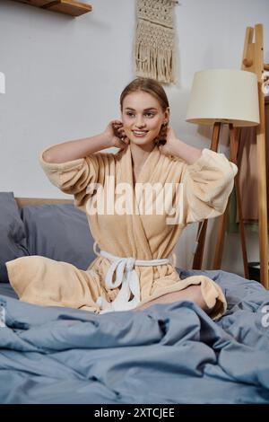 Eine junge Frau in einem Plüschmantel sitzt bequem auf einem Bett und genießt die friedliche Atmosphäre ihres Hauses. Stockfoto