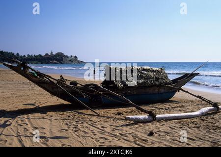 Traditionelles Holzfischboot mit Strohdach und Outtrider, mit Saman Villas in der Ferne, am Bentota Beach in der Nähe von Bentota, Südprovinz, Sri Lanka. Archivbild, das 2001 aufgenommen wurde Stockfoto