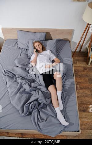 Eine junge Frau liegt im Bett und lächelt, während sie am Telefon spricht. Stockfoto