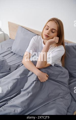 Eine junge Frau entspannt sich im Bett, die Augen geschlossen und der Kopf auf der Hand. Stockfoto