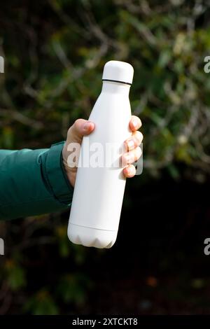 Der Mann hält eine Modell-Thermoskanne gegen verschwommene Büsche aus der Nähe Stockfoto