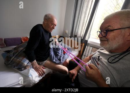 CHARKIV, UKRAINE - 13. AUGUST 2024 - ein älterer Mann übt mit einem Gummiband während einer Physiotherapie-Sitzung mit dem britischen Freiwilligen Brian Grove (R) in der Big Family Shelter der NGO durch den Krieg, die sich um allein ältere Menschen kümmert, die durch den Krieg obdachlos geworden sind, Charkiv, Nordost-Ukraine. Stockfoto