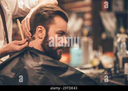 Das Haar sieht magisch aus. Nahaufnahme eines jungen bärtigen Mannes, der vom Friseur im Friseur mit Rasiermesser geschnitten wurde Stockfoto