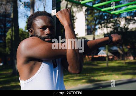 Schwarzer Mann im ärmellosen Hemd im Park, der vor dem Training Sport-Aufwärmen zur Vorbeugung von Gelenkverletzungen macht. Stockfoto