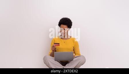 Geschäftsfrau mit Kreditkarte, die Online-Shopping über Laptop macht, während sie auf weißem Hintergrund sitzt Stockfoto