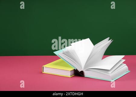 Bunte Bücher auf rosa Tisch vor grünem Hintergrund, Platz für Text Stockfoto