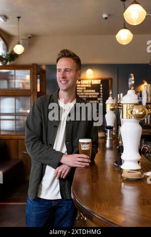 Luke Boase, Gründer und CEO der alkoholfreien Biermarke Lucky Saint, fotografierte mit seinem alkoholfreien Bier in einem Londoner Pub in England, Großbritannien Stockfoto