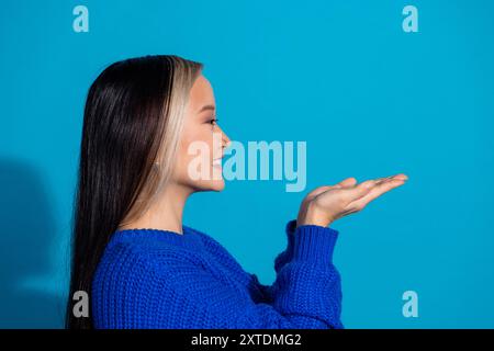 Foto-Porträt der schönen jungen Dame Profil halten leeren Raum gekleidet stilvolle Strickkleidung Kleid isoliert auf blauem Hintergrund Stockfoto